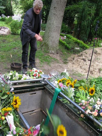 Jan werpt nog 2 zonnebloemen in het graf